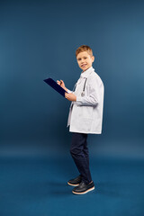 A preadolescent boy in a lab coat holding a clipboard.