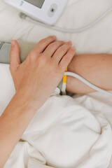 Person lying in bed with blood pressure monitor and cuff on arm, healthcare concept