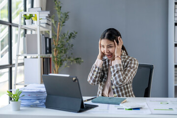 A woman is sitting at a desk with a laptop and a stack of papers