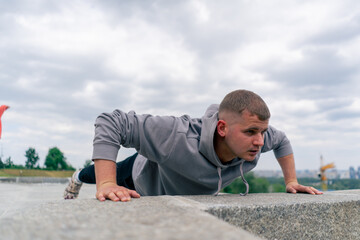 in the park, a young guy in a gray hoodie is doing a warm-up doing push-ups on the camera healthy lifestyle cloudy weather