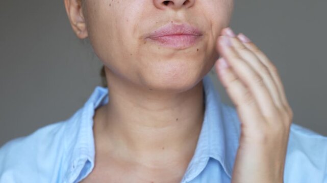 Bad breath. A young caucasian woman checking her breath by blowing on her hand on a grey background. Diseases of the teeth or gastrointestinal tract