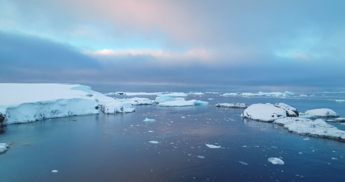 Sunset over Antarctica ocean coast winter landscape. Aerial flight over cold polar water ice floes. Ecology, melting ice, climate change, global warming. Wild nature background, South Pole travel