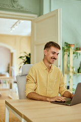 Fototapeta premium Smiling man working over the laptop, typing some e-mails.