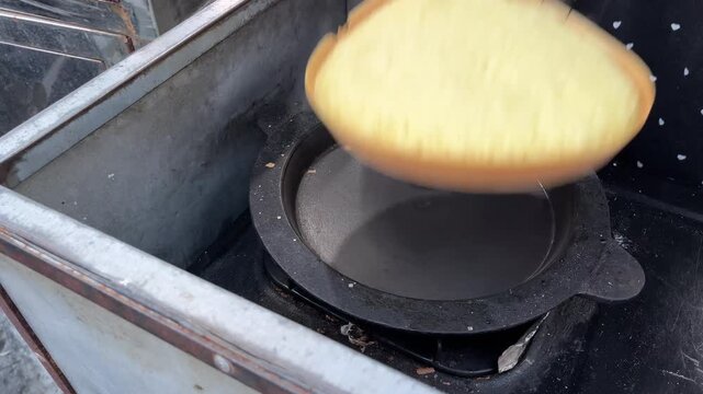 A person makes Indonesian dessert Terang Bulan, pouring batter onto a griddle and adding toppings. The process shows the dessert's golden crust and delicious fillings