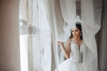 Fototapeta premium A bride is standing in front of a window with a veil covering her face. She is wearing a white dress and a tiara