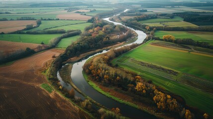 Showcase an aerial view of a river winding through a rural landscape, highlighting the patchwork of fields and forests