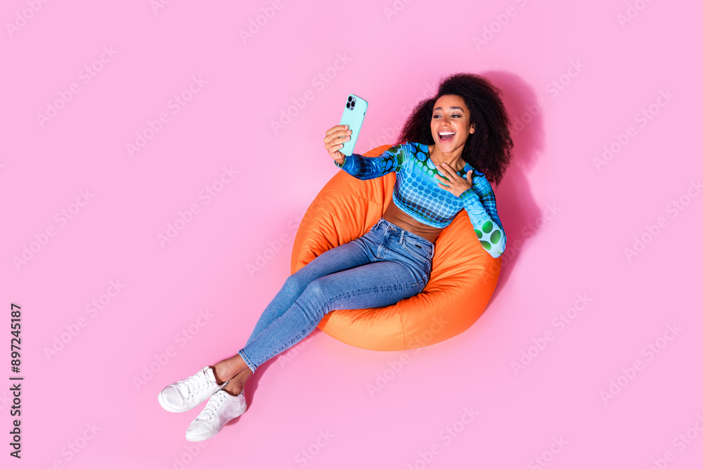 Poster Full size photo of lovely young lady sit orange beanbag video call talking dressed stylish blue garment isolated on pink color background