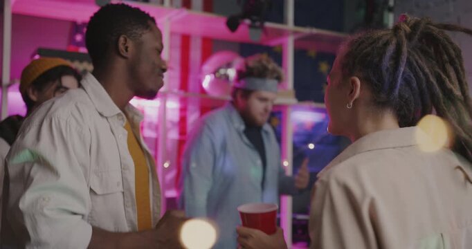 Cheerful young people friends dancing holding cups with drinks relaxing at enjoyable night party at home. Leisure and youth culture concept.