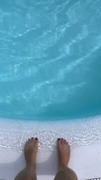 Girl's feet on the curb of the blue water pool
