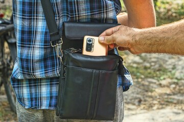 the hand of a thief pulls out a modern mobile phone from the back of a man dressed in a blue...