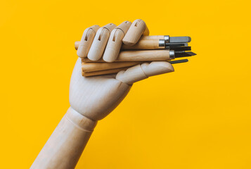 A wooden artificial mannequin hand holds a set of linocut cutters on a yellow background. The...