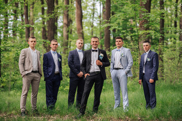 A group of men in suits are posing for a photo in a forest. Scene is formal and relaxed, as the men are dressed in suits and ties, but they are also standing in a natural setting