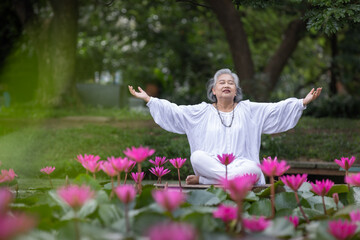 Elderly Woman Sitting Peacefully on Dock Surrounded by Blooming Pink Lotus Flowers in Pond