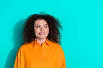 Fototapeta premium Photo of positive woman with wavy hairstyle dressed orange t-shirt look empty space biting lip isolated on turquoise color background