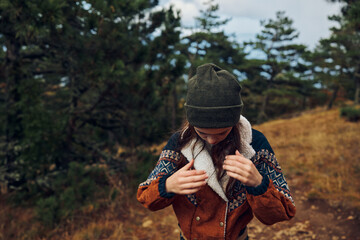 Fototapeta premium A young woman in a stylish hat and jacket standing on a serene dirt road in the peaceful woods, embodying beauty and nature