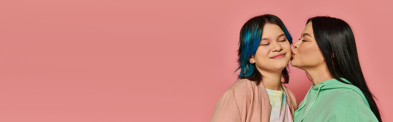 An Asian mother and her teenage daughter stand side by side, exuding elegance in casual wear against a pink studio background.