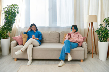 Obraz premium An Asian mother and her teenage daughter sit on a couch in a living room, spending time together in casual wear.