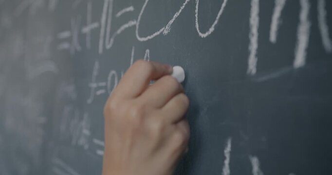Close-up slow motion of female hand teacher writing symbols on chalkboard teaching physics in high school. Education and science concept.