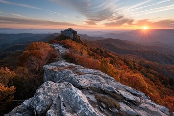 Fototapeta premium The photo showcases a rocky mountain range bathed in the glow of a stunning sunset, with vibrant red and orange autumn trees and a dramatic, open sky above.