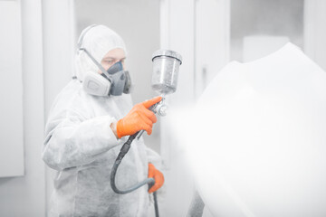 Professional male car painter is painting in garage by airbrush. Worker paints vehicle with spray gun.