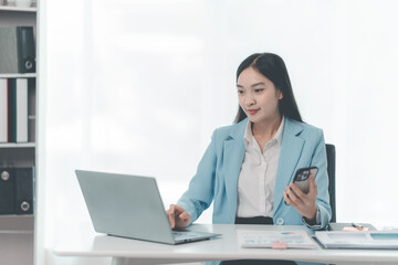 Asian businesswoman using laptop and talking on mobile phone Contact financial businesses online, talk to customers on the phone with a confident demeanor and effective communication skills.