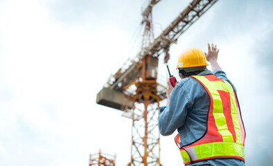 Portrait of crane worker uses walkie-talkie communicate with tower crane operators to lift and move...