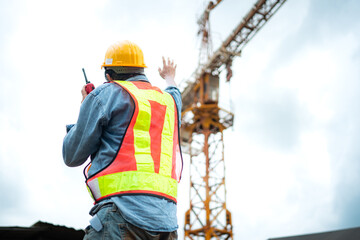 Portrait of crane worker uses walkie-talkie communicate with tower crane operators to lift and move objects on building construction sites