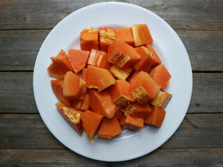 Top view of papaya pieces on white plate with grey plank background