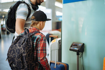 caucasian bearded man with son in airport putting suitcase on weights mesuring luggage