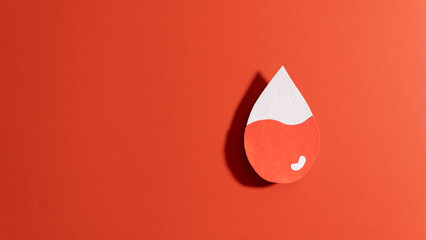 Blood drop with low blood level made from paper on red background. Concept of hematologic disorders...