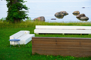 White and brown wooden benches by the sea. Green grass. Stones in water on the back. Concept of rest and relax. Summertime. Tallinn, Estonia, July 2024