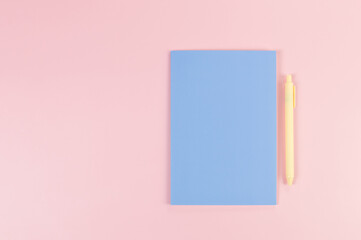 Top view of blue notebook, yellow pen on pink background. School, office wallpaper. Flat lay, copy space.