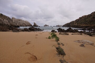 Scenic view of a rocky beach with footprints in the sand and a cloudy sky