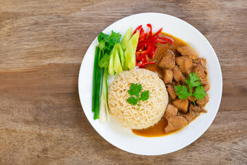 Chinese style chicken gravy fragrant with sesame oil and steamed jasmine brown rice with side dishes of scallions, cucumber, cilantro, red chilli in white plate on wooden table.