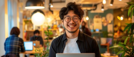 Excited Japanese man smiling and holding his laptop in a vibrant coworking space celebrating a significant achievement