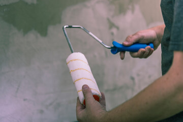 A close-up view of a hand holding a paint roller with a blue handle and a white, yellow-striped...