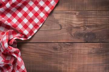 A rustic wooden table with a red and white checkered tablecloth partially draped over it, creating a cozy and inviting atmosphere for a meal or picnic.
