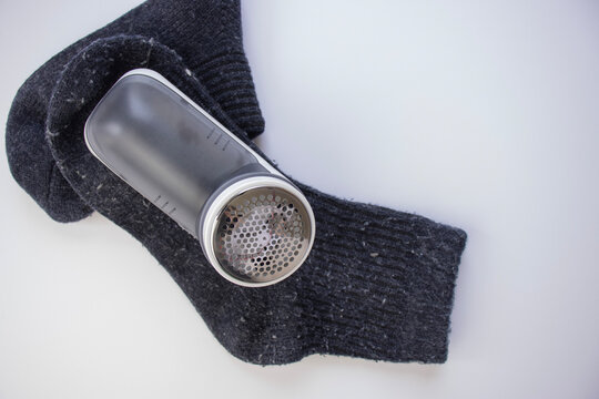 Close-up of a fabric shaver. Knitted socks with wool scraps. Shaving fabric. Top close-up view. Blue wool socks on white background