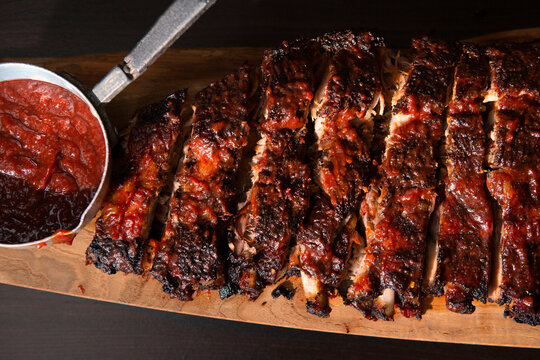 Sliced Rack of Pork Spareribs with side of BBQ Sauce on Wooden Board
