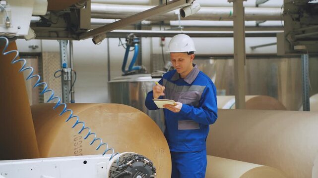 Engineer at factory for production of corrugated cardboard from paper checks technical condition of equipment before starting. Technical supervision controls compliance with standards, operating rules