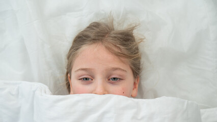 Top view of a little girl hiding under a blanket. 