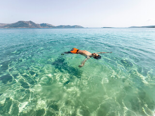 A young boy floats effortlessly in crystal-clear turquoise water, with his arms outstretched and a serene expression on his face.