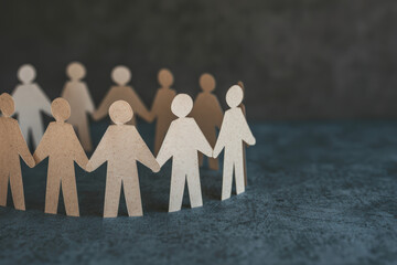 Paper cutout people standing in a circle holding hands, symbolizing community, teamwork, collaboration, and unity on a dark textured background.
