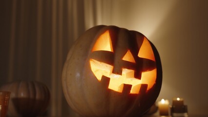 Pumpkin with a Carved Halloween Jack-o'-Lantern Symbol, Fire Burning Inside It, in a Dark Room on the Table with Pumpkins and Candles. Warm Tones of Home Interior.