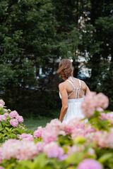 caucasian woman from behind, walking through her garden with pink hydrangea bushes in the foreground