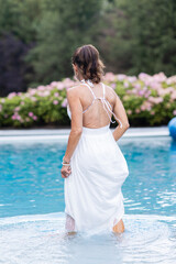 fit woman in white dress stepping into her pool with greenery and hydrangea bush in background on...