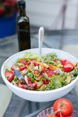 healthy delicious summer salad with sliced strawberries and greens in large white bowl on outdoor table 