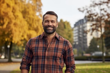 Fototapeta premium Portrait of a satisfied man in his 40s dressed in a relaxed flannel shirt on vibrant city park