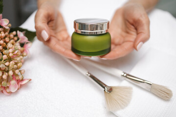 cosmetologist holds a green jar of cream in her hands