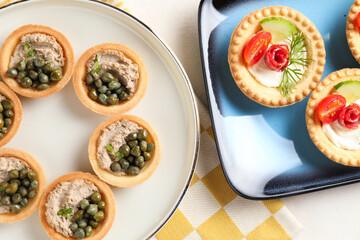 Delicious canapes with pate, dry smoked sausages and capers on light table, flat lay